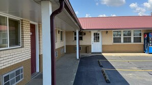 A motel with a covered parking area and a red-roofed building in the background.