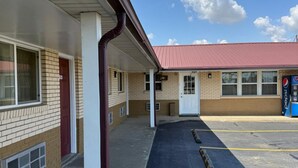 A motel with a covered parking area and a red-roofed building in the background. - Deluxe Inn (Hebron)