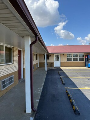 A motel with a covered parking area and a red-roofed building in the background. - Deluxe Inn (Hebron)
