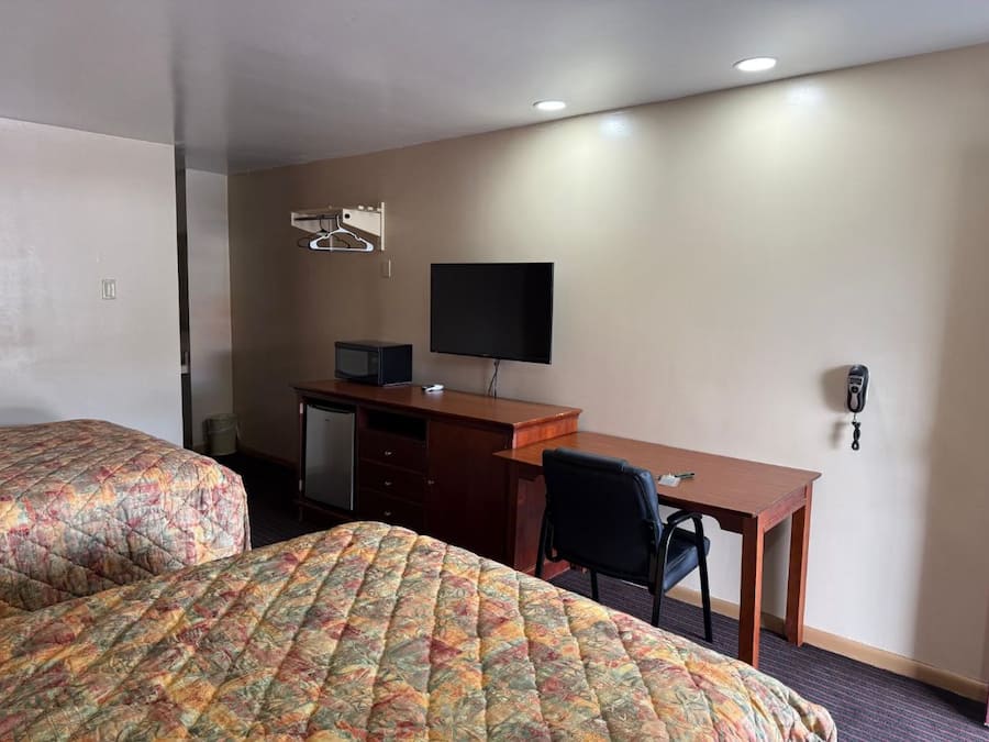 Quarto de hotel com duas camas, uma escrivaninha, uma cadeira, uma televisão e um telefone.