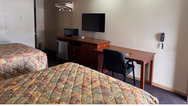 A hotel room with two beds, a desk, a chair, a television, and a telephone.