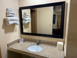 Un baño con lavamanos, espejo y toallas colgadas en la pared.