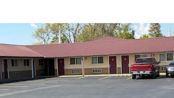 A motel with a red roof and beige walls, featuring a parking lot and a red pickup truck parked in front.