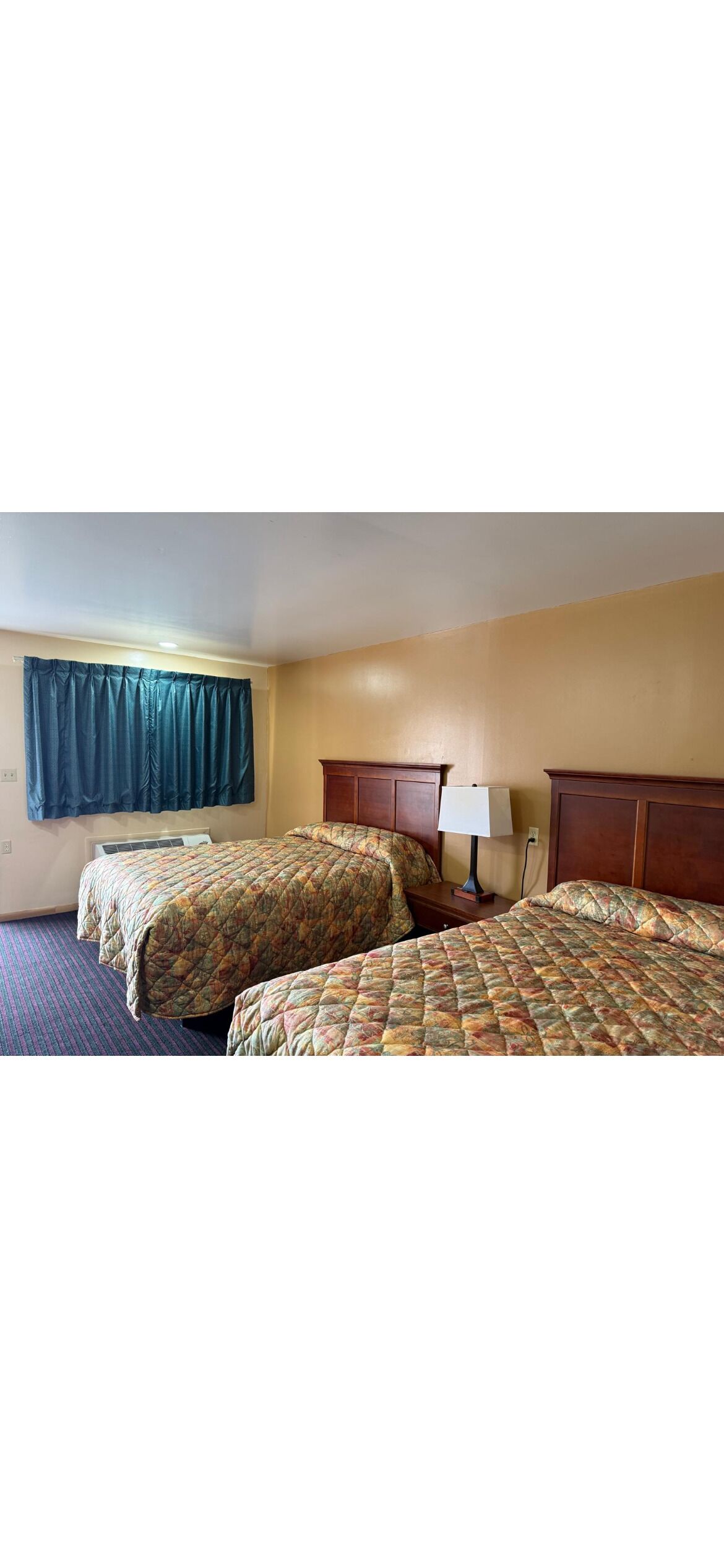 Habitación de hotel con dos camas, una mesita de noche con lámpara y una ventana con cortinas.