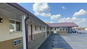 A motel with a row of rooms, a parking lot, and a small building in the background.