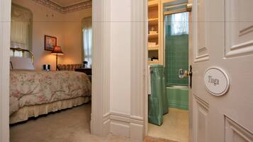 A bedroom with a floral bedspread, a bedside lamp, and a green bathroom visible through an open door.