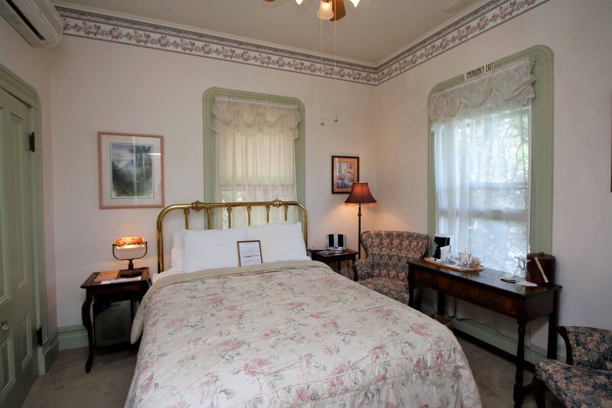 A bedroom with a large bed, a chair, a desk, and a window with curtains.