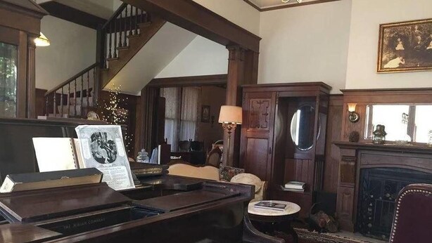 A grand piano in a spacious room with a staircase, a fireplace, and a chandelier. - Bradford Place Inn & Gardens (Sonora)