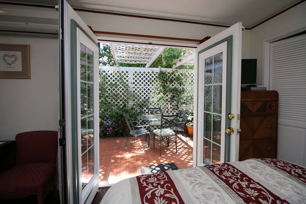 A bedroom with an open door leading to a patio with a table and chairs, a wooden dresser, and a red chair.