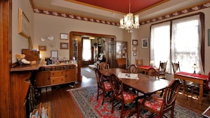 A dining room with a large wooden table, chairs, and a chandelier. There is a red carpet and a wooden cabinet with drawers. - Bradford Place Inn & Gardens (Sonora)