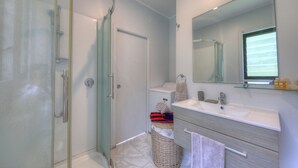 Un baño moderno con cabina de ducha de vidrio, inodoro, lavamanos con espejo y una cesta de mimbre.