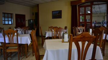 A dining area with tables and chairs, a painting on the wall, and a door leading to another room.