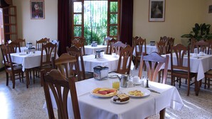 Un espace repas avec plusieurs tables et chaises, des articles pour le petit-déjeuner et une grande fenêtre avec des rideaux.