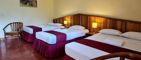 A hotel room with three beds, wooden headboards, a painting on the wall, and a tiled floor.