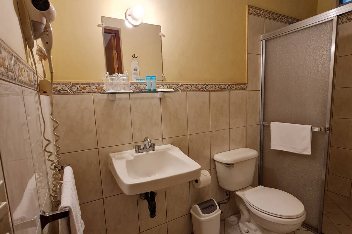 A bathroom with a sink, toilet, and shower. There is a towel rack and a hairdryer on the wall.