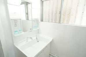 Un baño blanco con lavamanos, espejo y ventana con vidrio esmerilado.