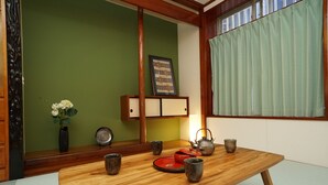 Ein traditioneller japanischer Raum mit Tatami-Boden, einem Holztisch mit Tee-Service, einer Vase mit Blumen und einem Shoji-Bildschirm.