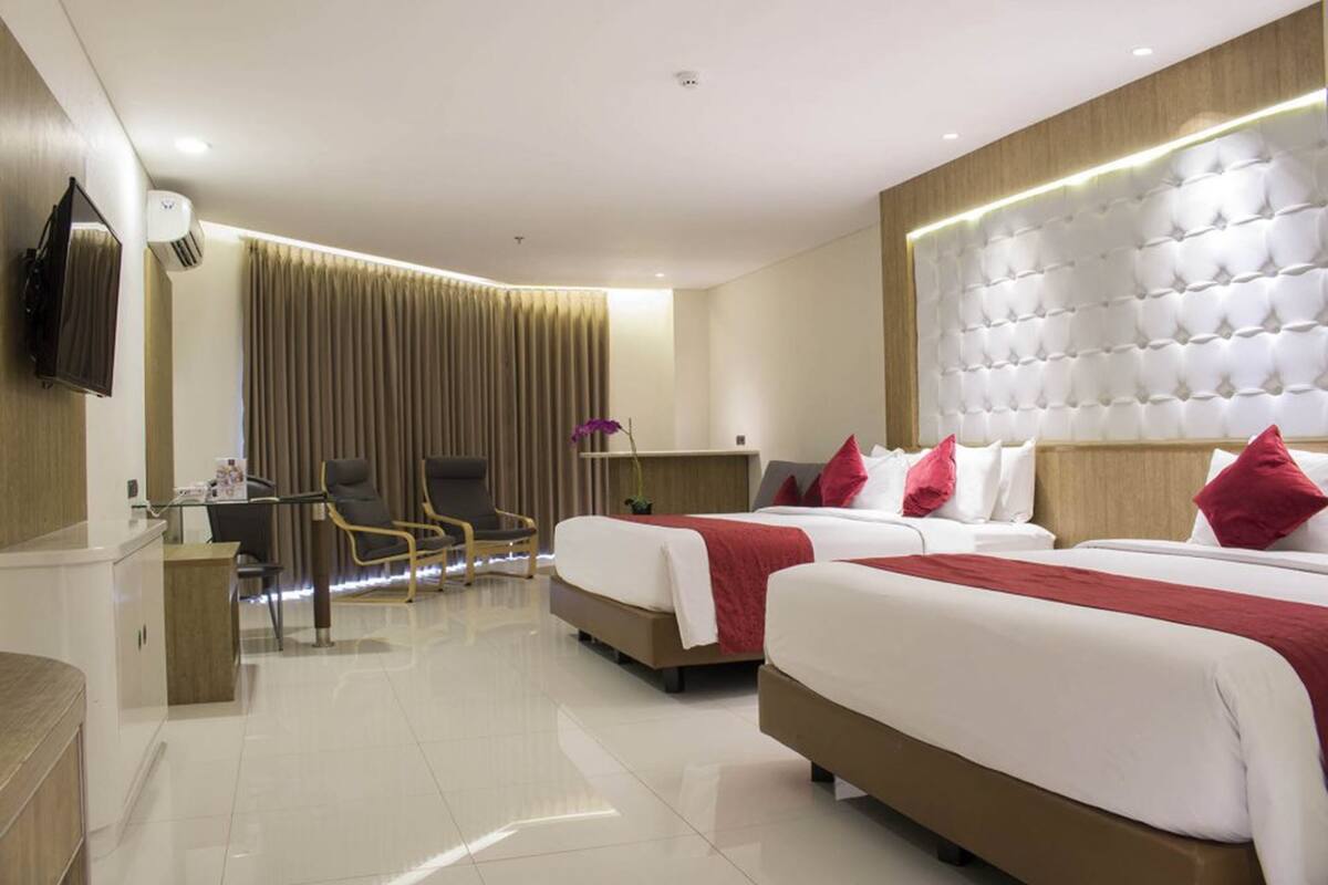 A hotel room with two beds, a desk, a chair, and a TV mounted on the wall.