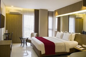 Habitación de hotel con una cama grande, una mesita redonda pequeña, una silla, un escritorio y un televisor montado en la pared.