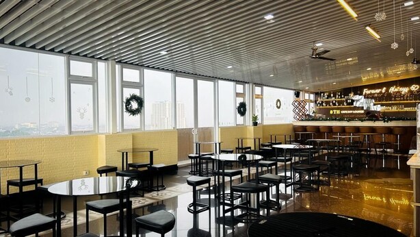 Un café moderne doté de nombreuses tables et chaises, d’un bar et de grandes fenêtres ornées de guirlandes décoratives.