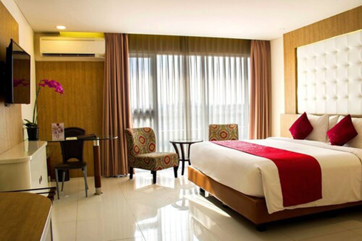 A hotel room with a bed, a desk, a chair, a small table, and a TV.