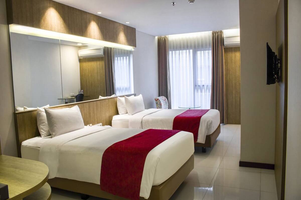 A hotel room with two beds, a round table, a large mirror, and a television.