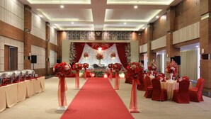 Une salle de banquet avec une allée recouverte d’un tapis rouge, des tables avec des chaises rouges et des compositions florales en guise de centre de table.