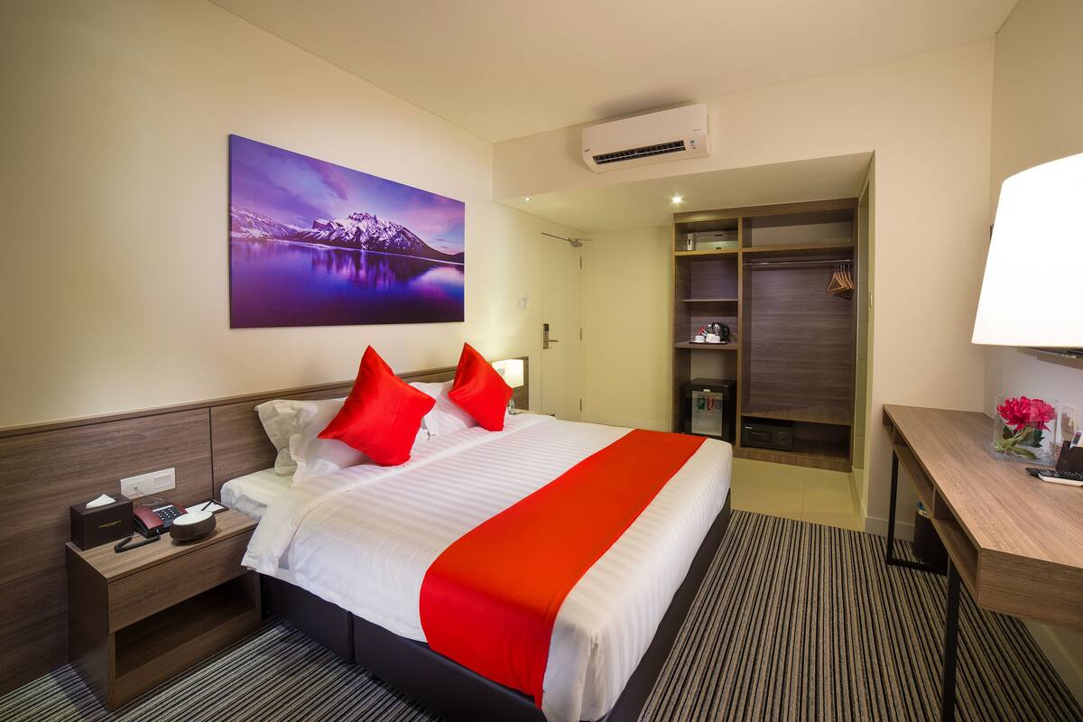 A hotel room with a large bed, a desk, a wardrobe, and a painting of mountains.
