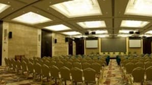 Une salle de conférence avec des rangées de chaises, un sol recouvert de moquette et un plafond haut doté de lucarnes.