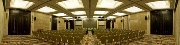 A conference room with rows of chairs, a carpeted floor, and a high ceiling with skylights.