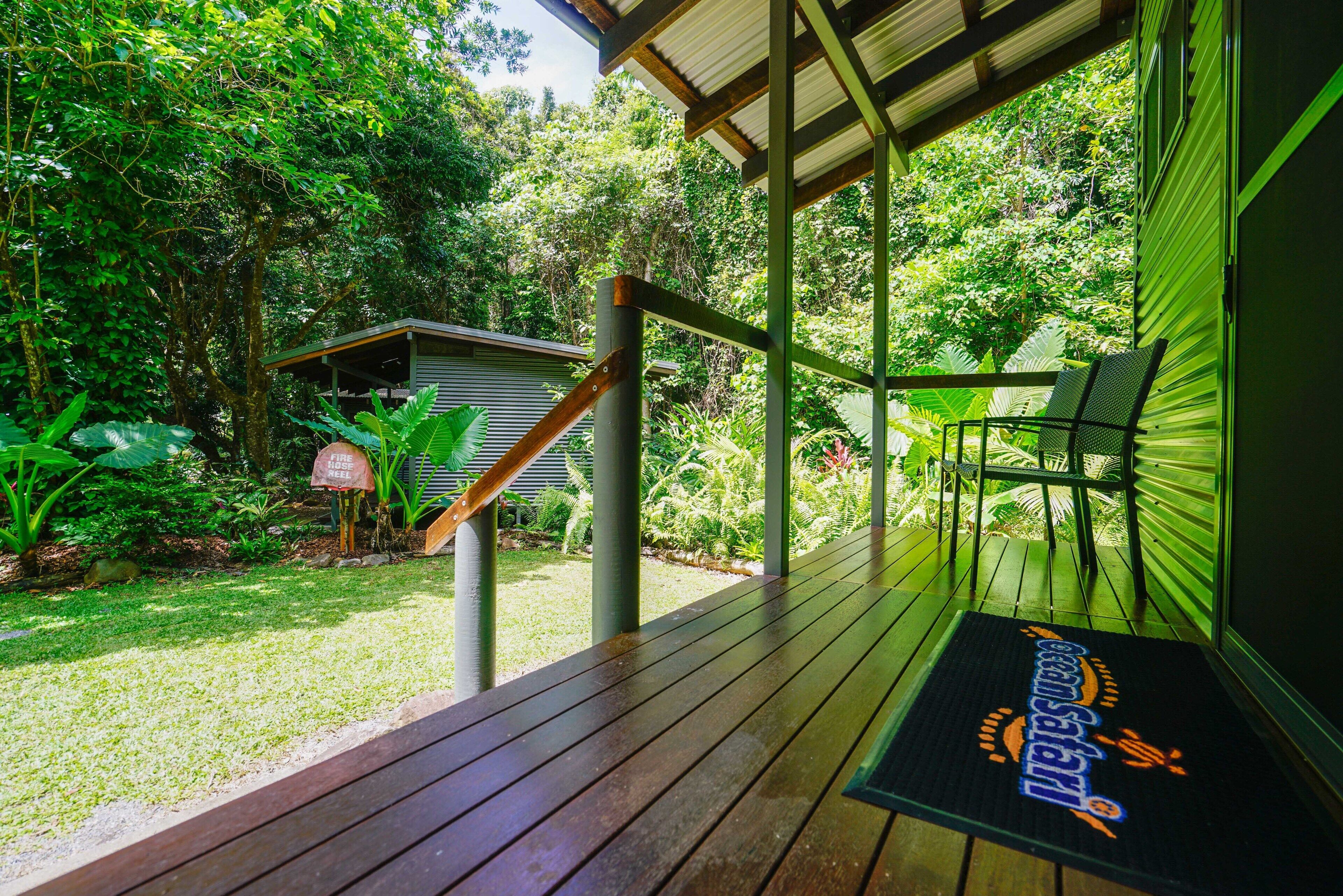 A wooden deck with a green railing, a small shed, and lush greenery in the background.