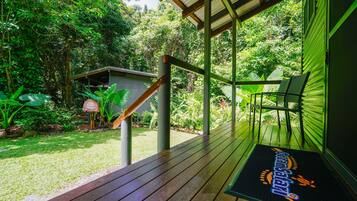 A wooden deck with a green railing, a small shed, and lush greenery in the background.