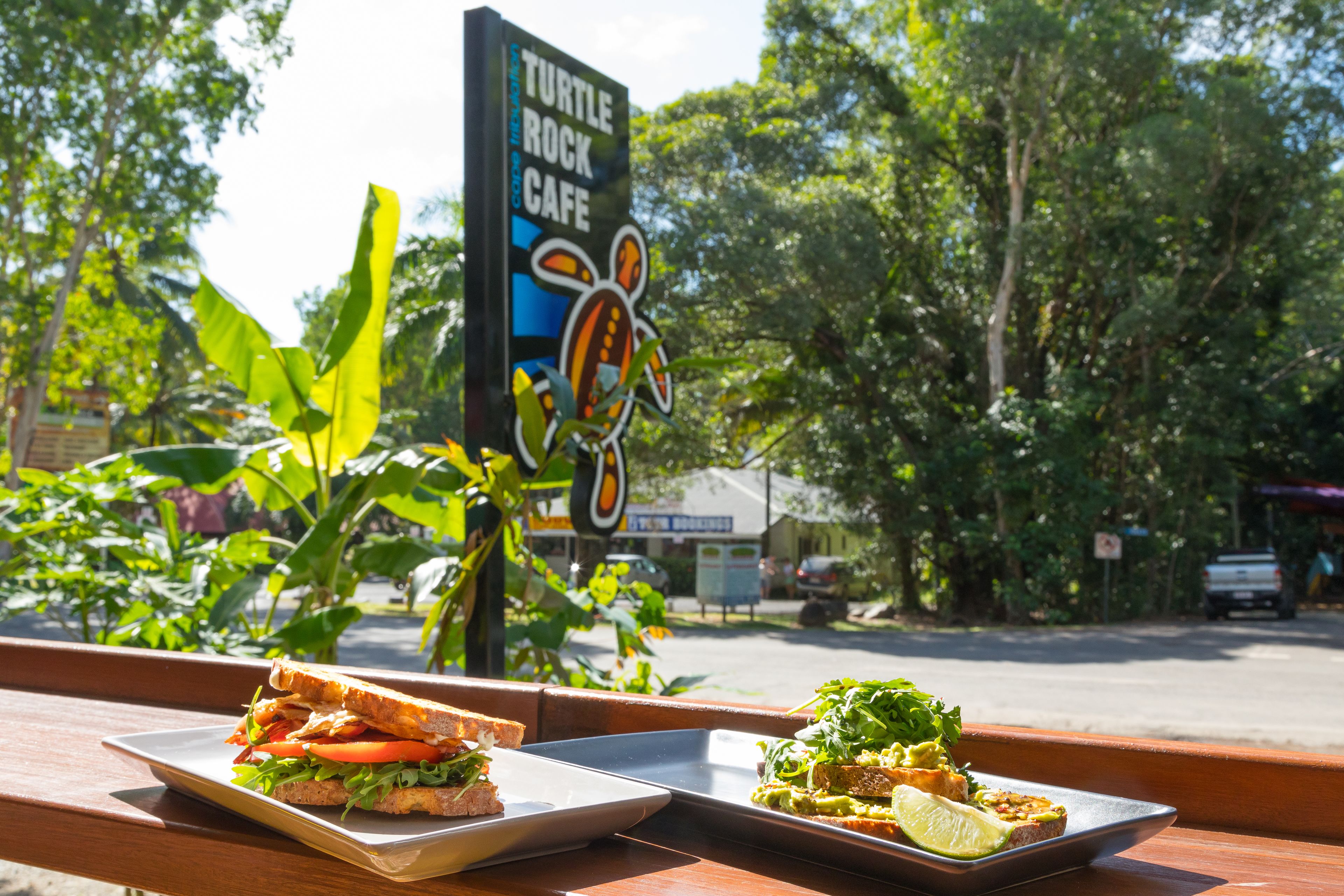 A sandwich and a plate of food on a wooden table with a sign for Turtle Rock Cafe in the background.