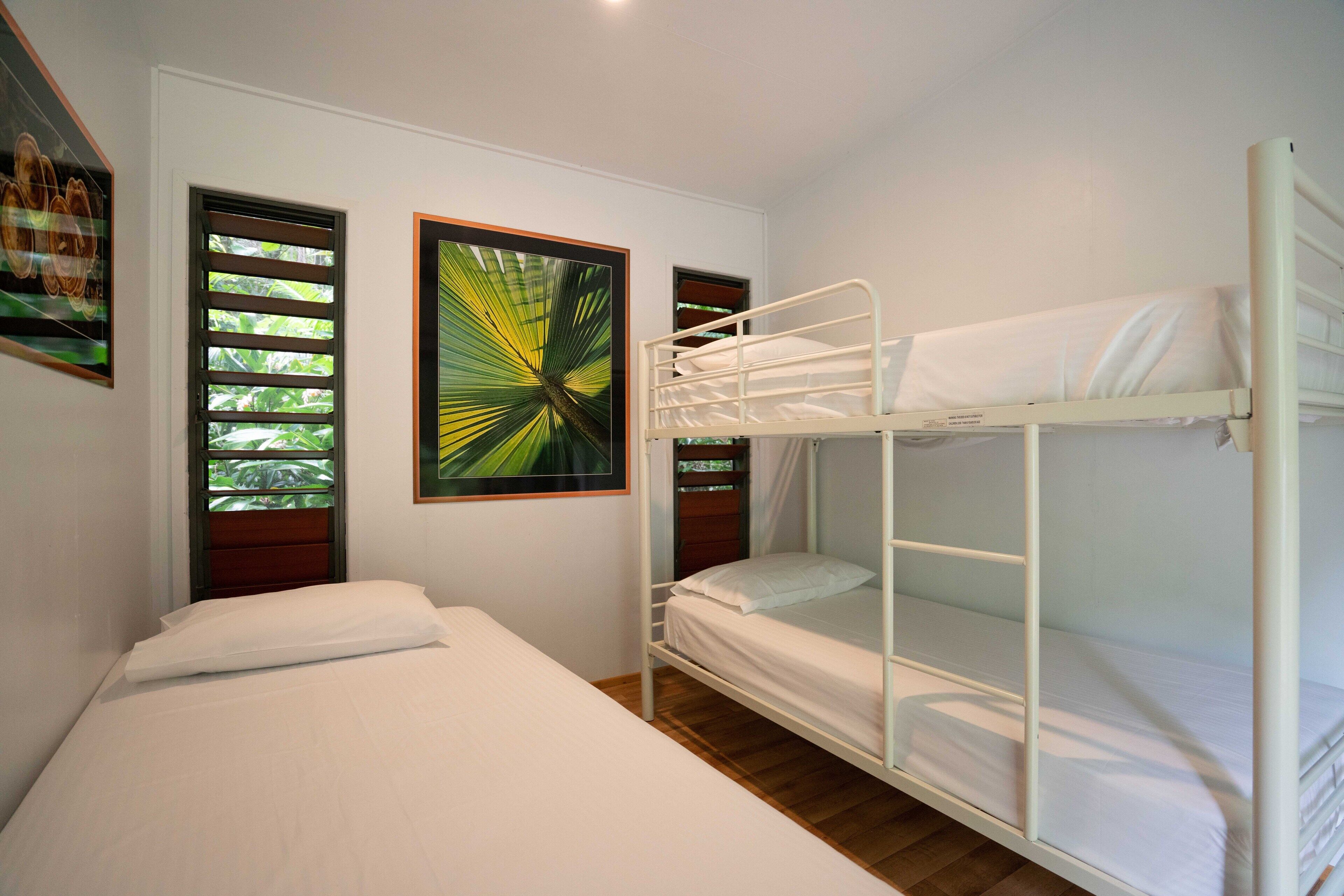 A room with a bunk bed, a single bed, and two framed pictures on the wall.