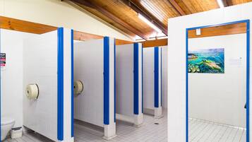 A restroom with white tiled walls, blue partitions, and a wooden ceiling.