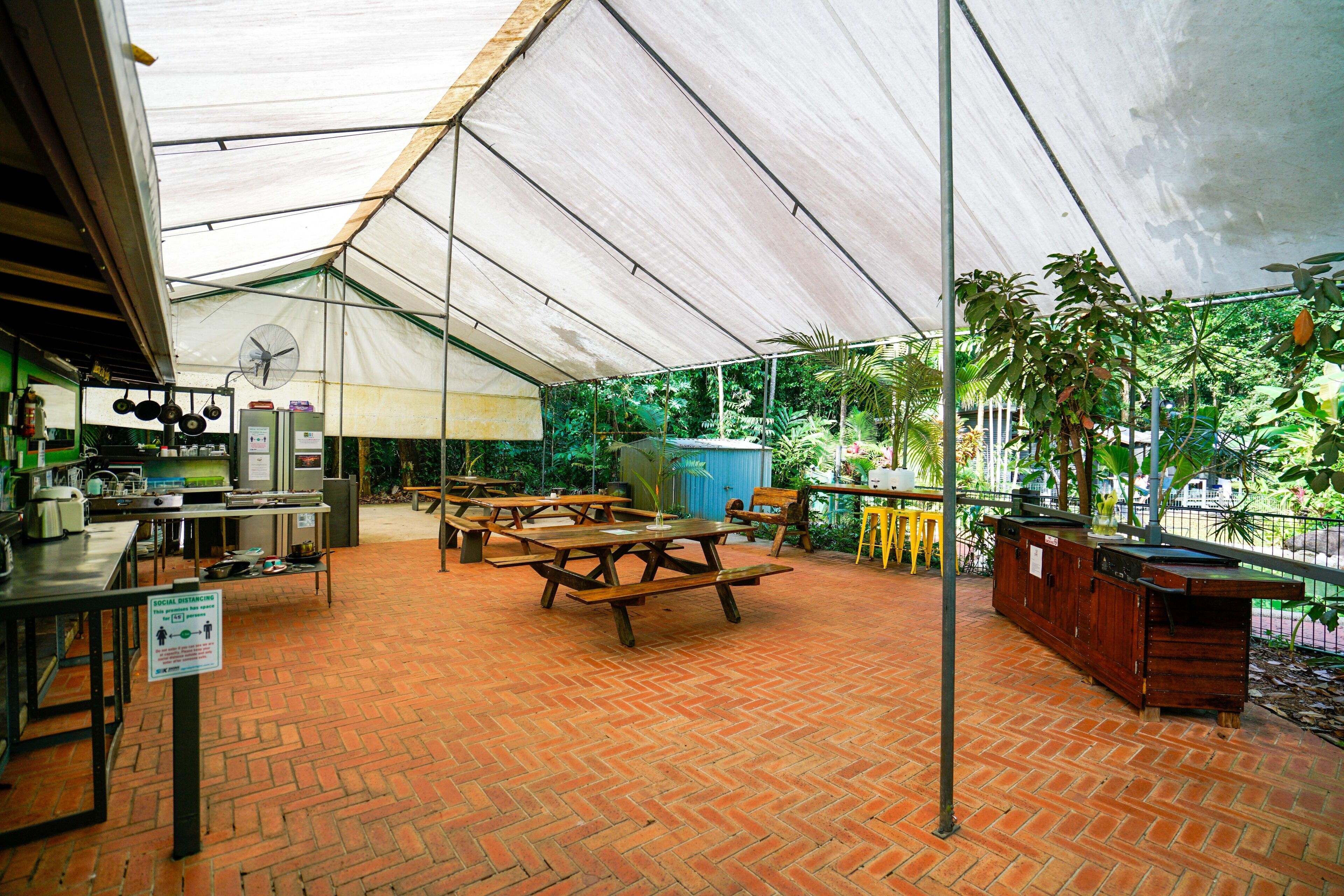 An outdoor patio with picnic tables, a grill, and a fan under a tent.