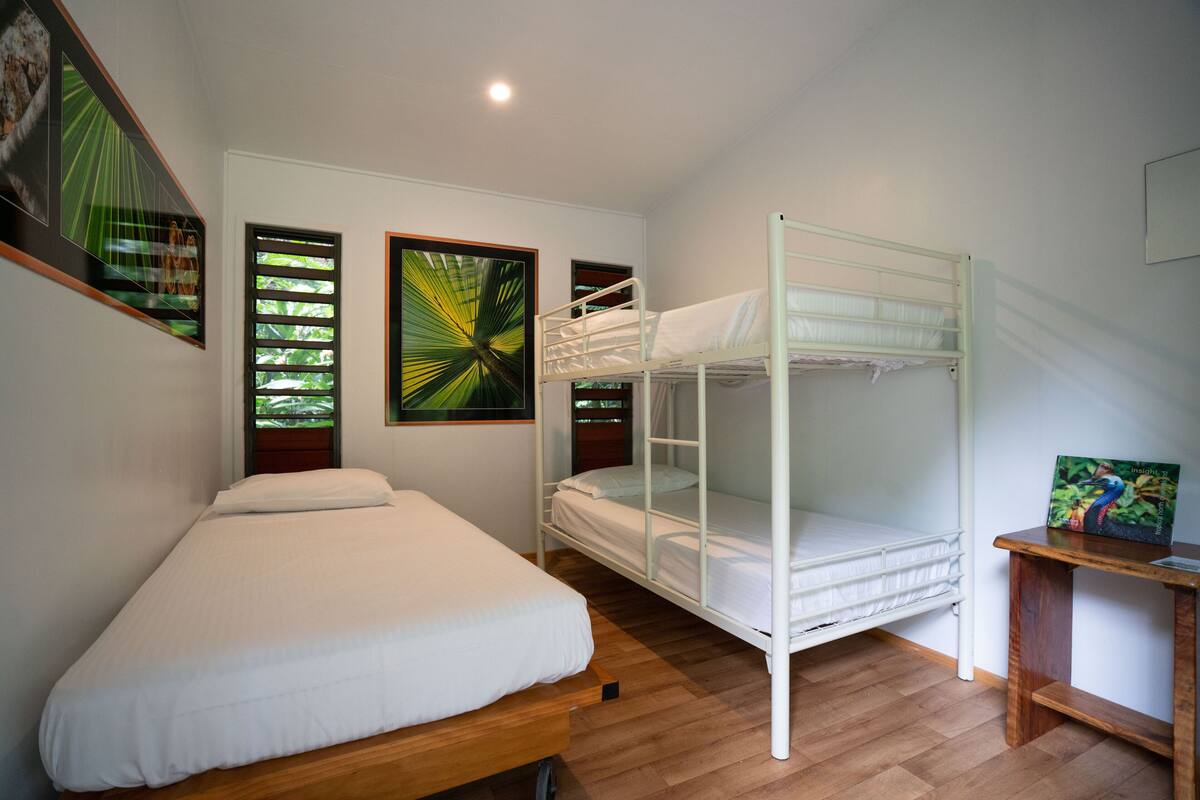 Ein Zimmer mit einem Einzelbett, einem Etagenbett, Holzboden und gerahmten Bildern an den Wänden.