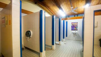 A public restroom with blue partitions, a hand dryer, a sink, and a ceiling fan.