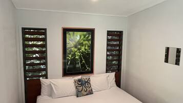 A neatly made bed with a brown quilt, a framed picture on the wall, and a small black book on the bed.