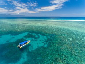 An aerial view of a clear blue sea with a boat on the surface. - Safari Lodge (Cape Tribulation)