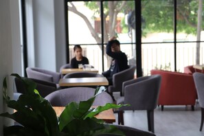 A modern indoor seating area with tables and chairs, large windows, and a potted plant in the foreground. - Sun Apartment (Phnom Penh)
