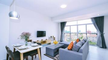 A modern living room with a dining area, a grey sofa, a flat-screen TV, and a large window with curtains.