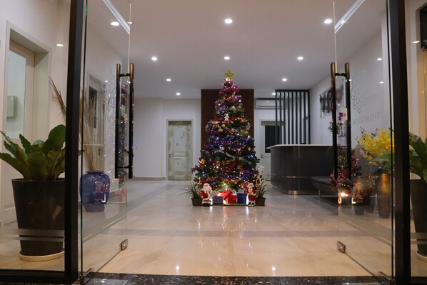 Un moderno vestíbulo de hotel con un gran árbol de Navidad adornado con luces y adornos, plantas en macetas y un mostrador de recepción.