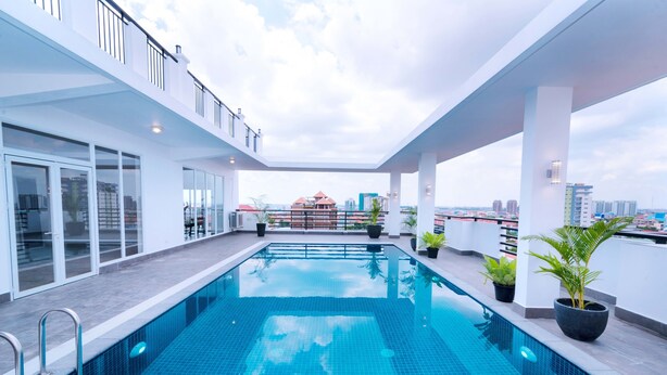 A rooftop swimming pool with glass railings and potted plants, surrounded by a white building with large windows. - Sun Apartment (Phnom Penh)