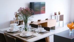 A modern dining area with a white table set for four, a vase with flowers, and a flat-screen TV mounted on the wall. - Sun Apartment (Phnom Penh)