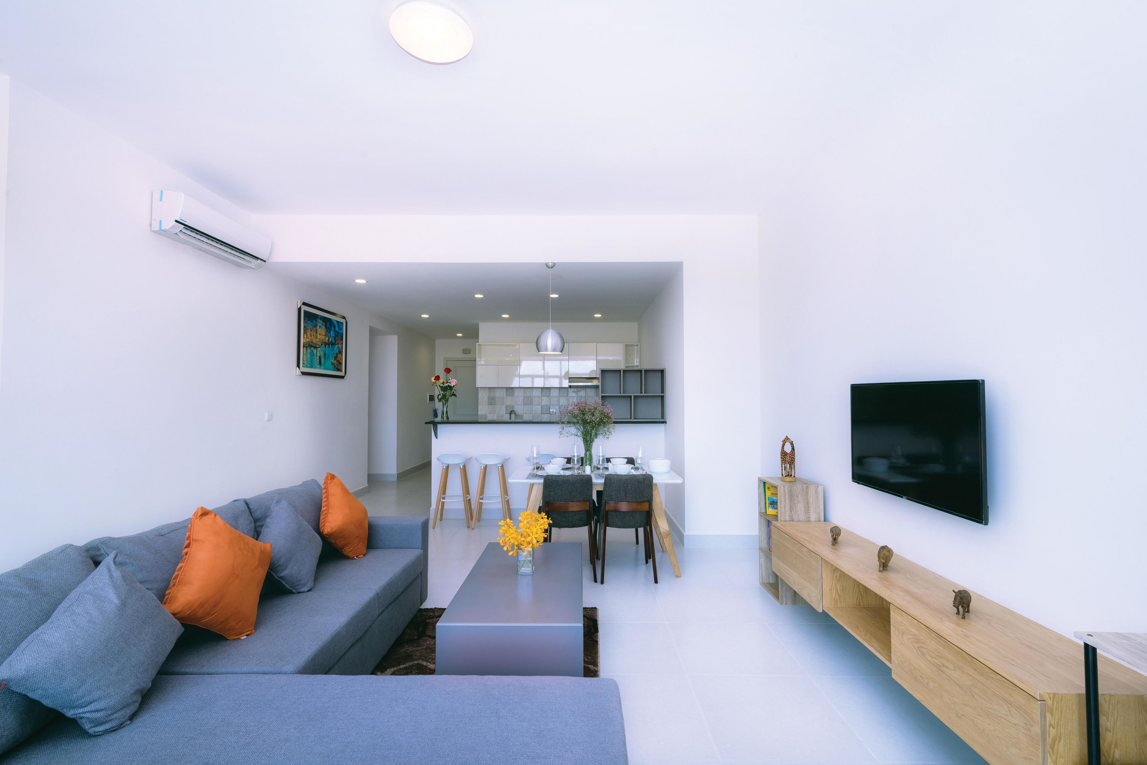 A modern living room with a grey sofa, orange cushions, a wooden coffee table, and a TV mounted on the wall.