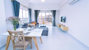 A modern living room with a dining area, a sofa, a TV mounted on the wall, and a balcony with a view of buildings. - Sun Apartment (Phnom Penh)