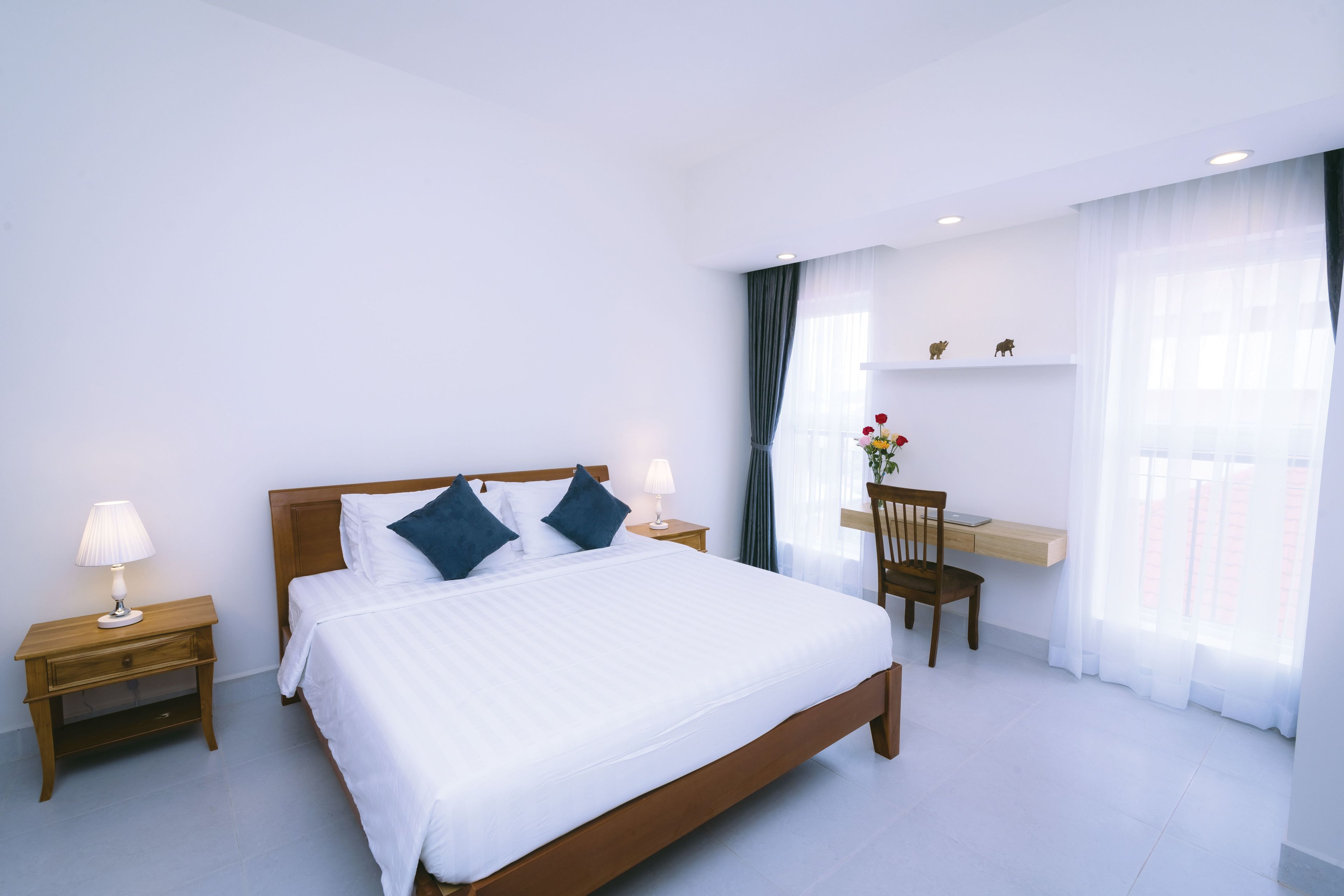Une chambre d’hôtel moderne avec un grand lit, des tables de chevet en bois, un bureau et une chaise.