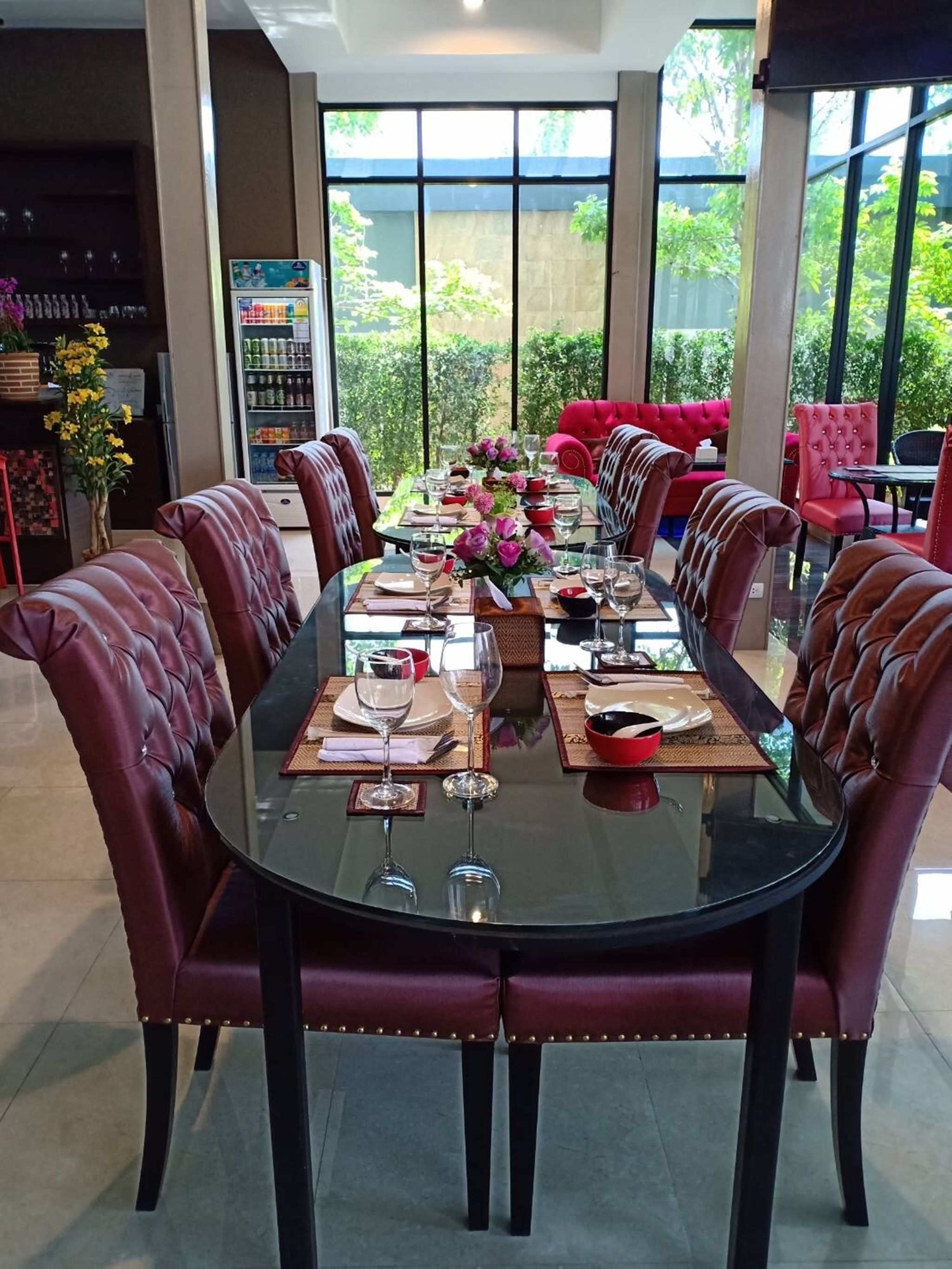 Zona pranzo con tavolo in vetro, sedie imbottite rosse e vista sulla vegetazione attraverso ampie finestre.