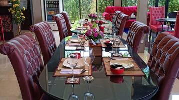 Zona pranzo con tavolo in vetro, sedie imbottite rosse e vista sulla vegetazione attraverso ampie finestre.